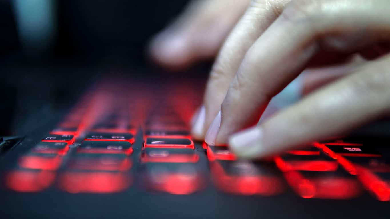 finger typing on a keyboard with red backlighting